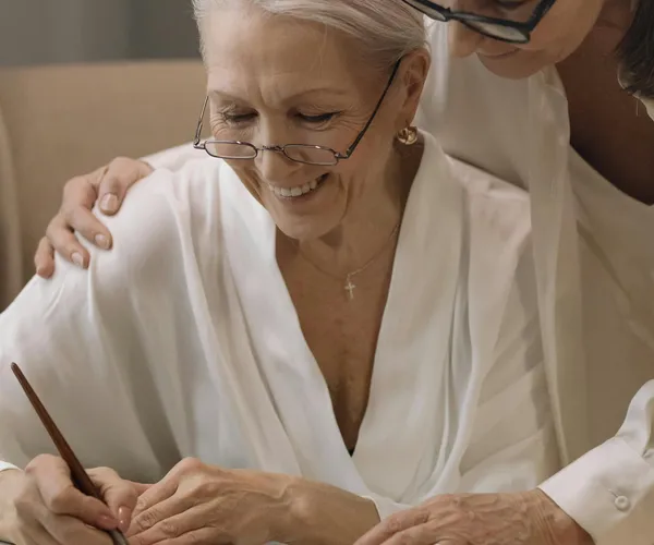 Caregiver helping elderly woman with writing activity during memory care